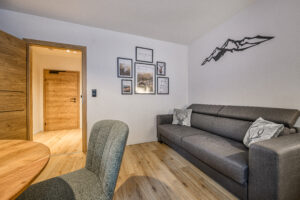 Wohnbereich der Ferienwohnung Daheim in Gastein mit Sofa, Alpendeko und Blick in den Flur.